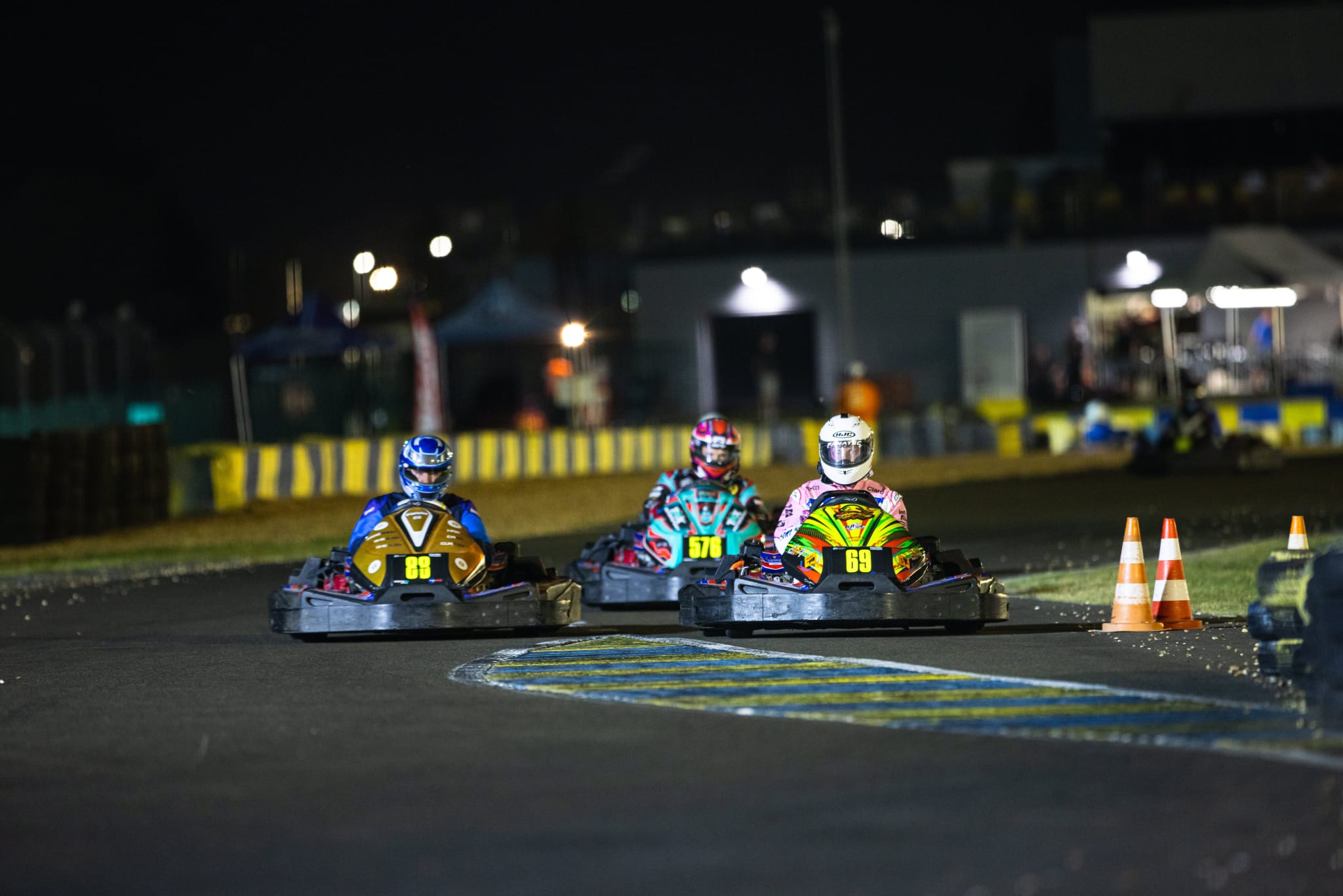Three go-karts battling wheel to wheel through a floodlit corner at night