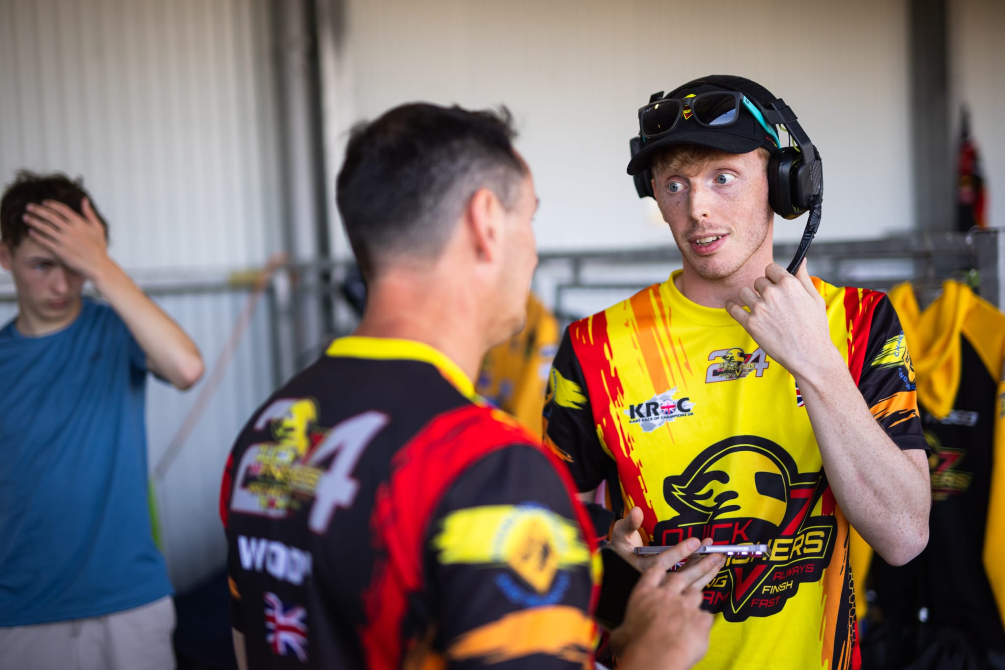 Racer wearing a headset and cap talking with a teammate in the pit garage