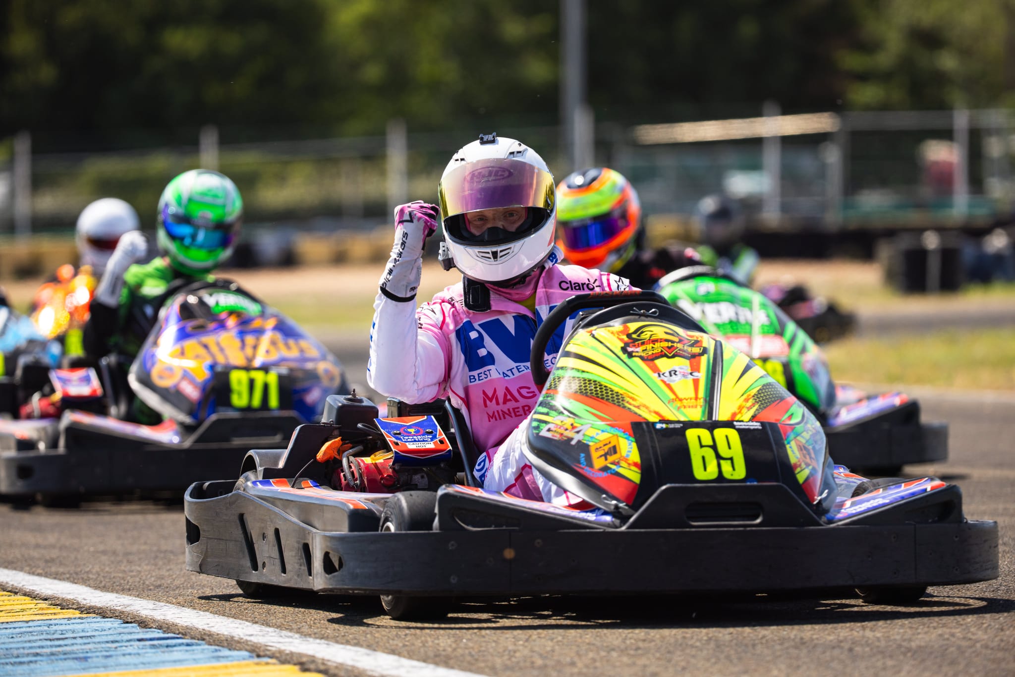 Karting driver in a colourful helmet battling wheel to wheel on track